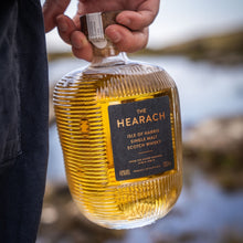 Load image into Gallery viewer, Person holding a bottle of The Hearach Isle of Harris Single Malt Scotch Whisky with a blurred natural background.