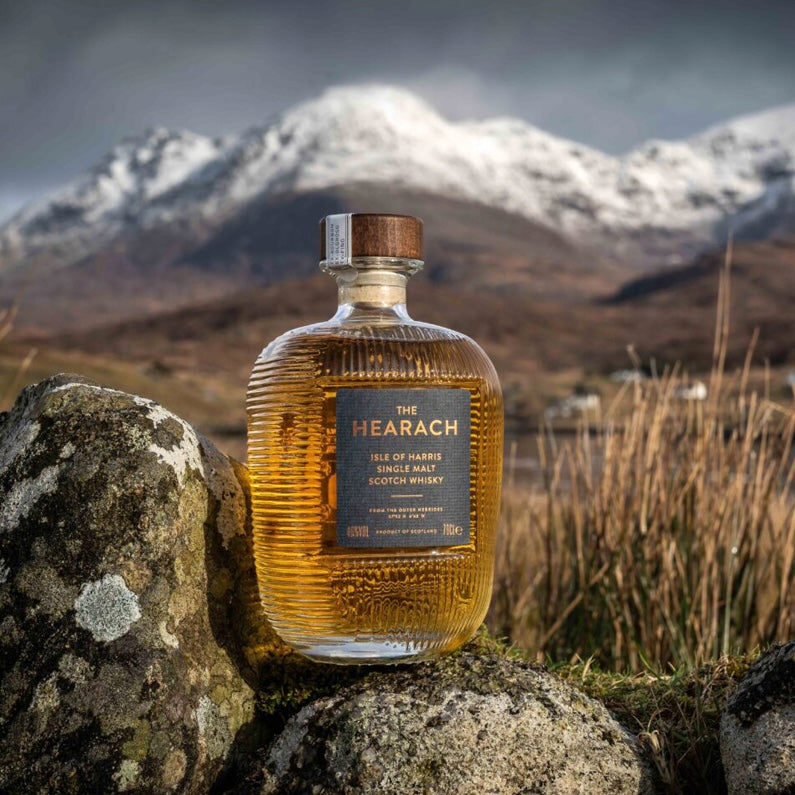 Load image into Gallery viewer, Isle of Harris 'The Hearach' Single Malt Whisky bottle on a rock infront of a mountain covered in snow