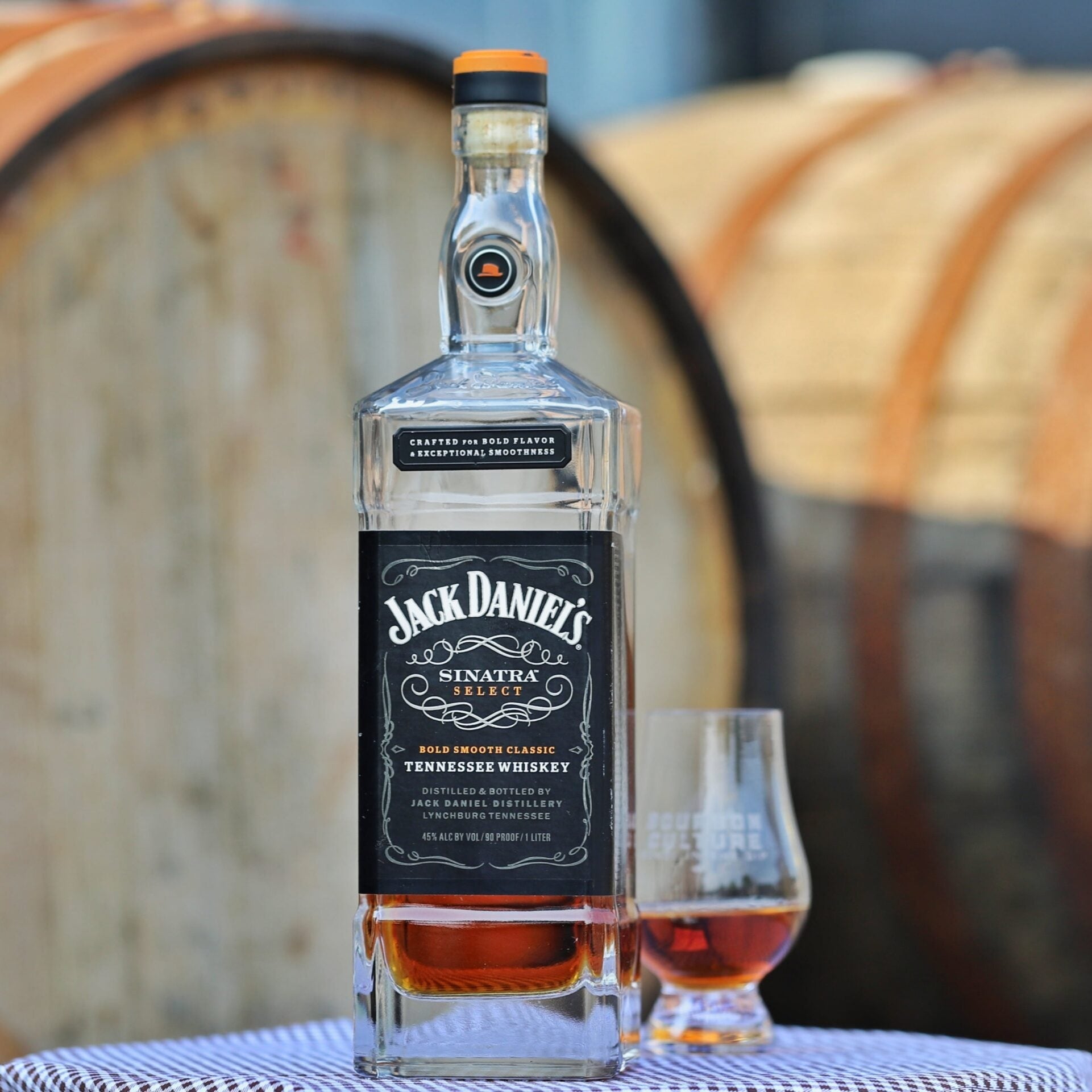 Load image into Gallery viewer, Jack Daniel's Sinatra Select Tennessee Whiskey bottle with a glass in front of wooden barrels.