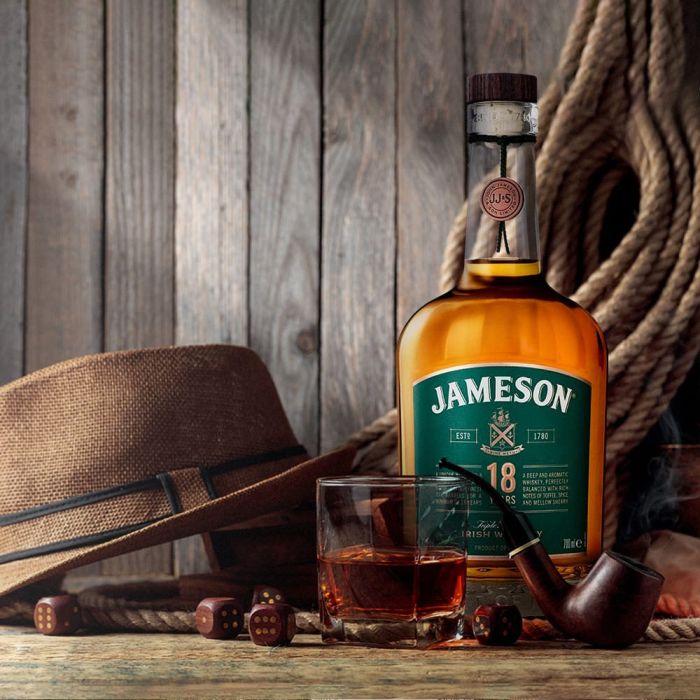 A bottle of Jameson 18 year old whiskey on a wood table with a tumbler and some dices rolling on the table