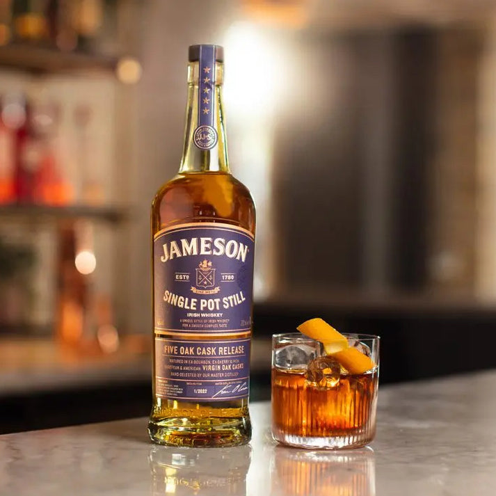 Load image into Gallery viewer, A bottle of Jameson Whiskey on a bar with a cocktail beside it and a blurry background of a bar