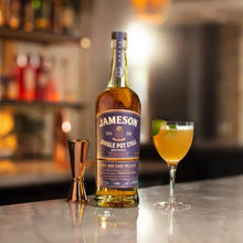 Load image into Gallery viewer, A bottle of Jameson Whiskey on a bar with a cocktail beside it and a blurry background of a bar