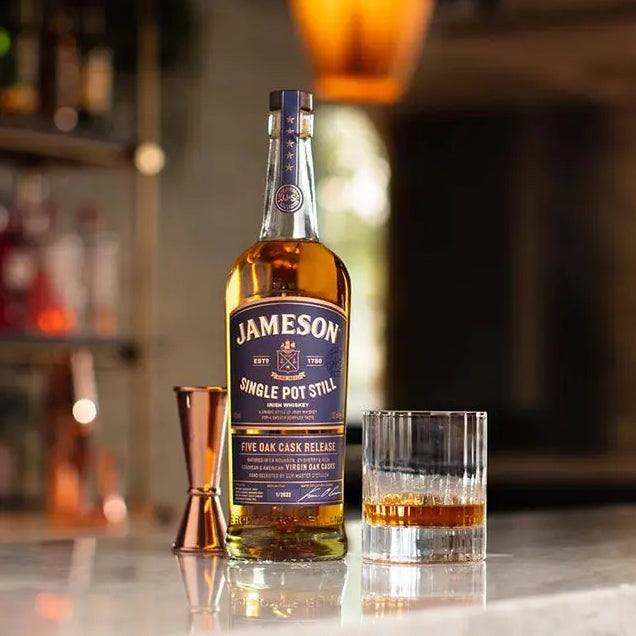 Load image into Gallery viewer, A bottle of Jameson Whiskey on a bar with a glass of neat whiskey beside it and a blurry background of a bar