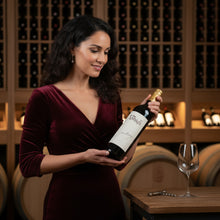Load image into Gallery viewer, Woman in a wine cellar holding a bottle of Jim-Barry-The-Armagh-Shiraz wine with a glass on a table.