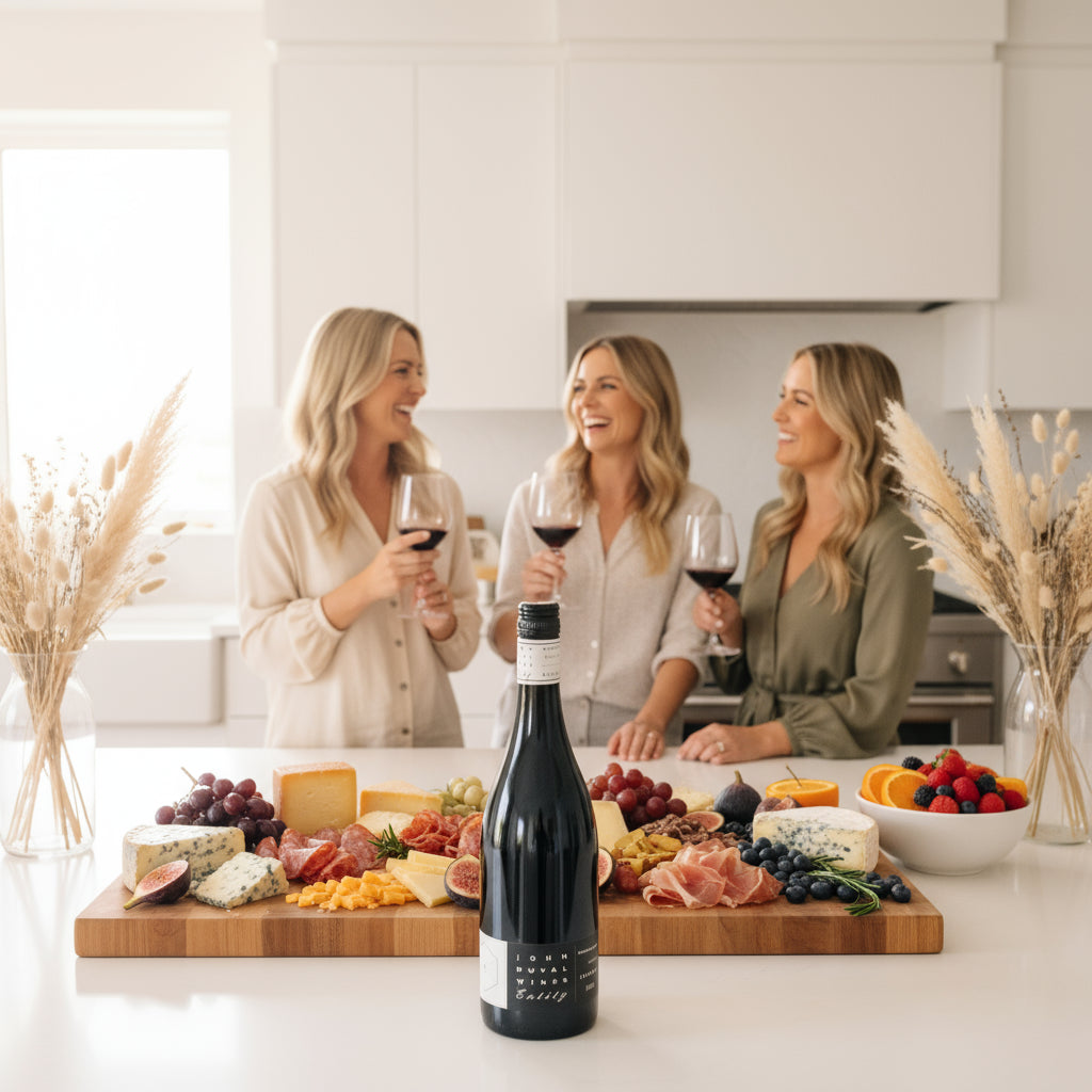 Three women enjoying John-Duval-Entity-Shiraz wine in a kitchen with a charcuterie board.