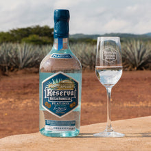 Load image into Gallery viewer, Bottle and glass of Reserva de la Familia tequila with agave plants in the background
