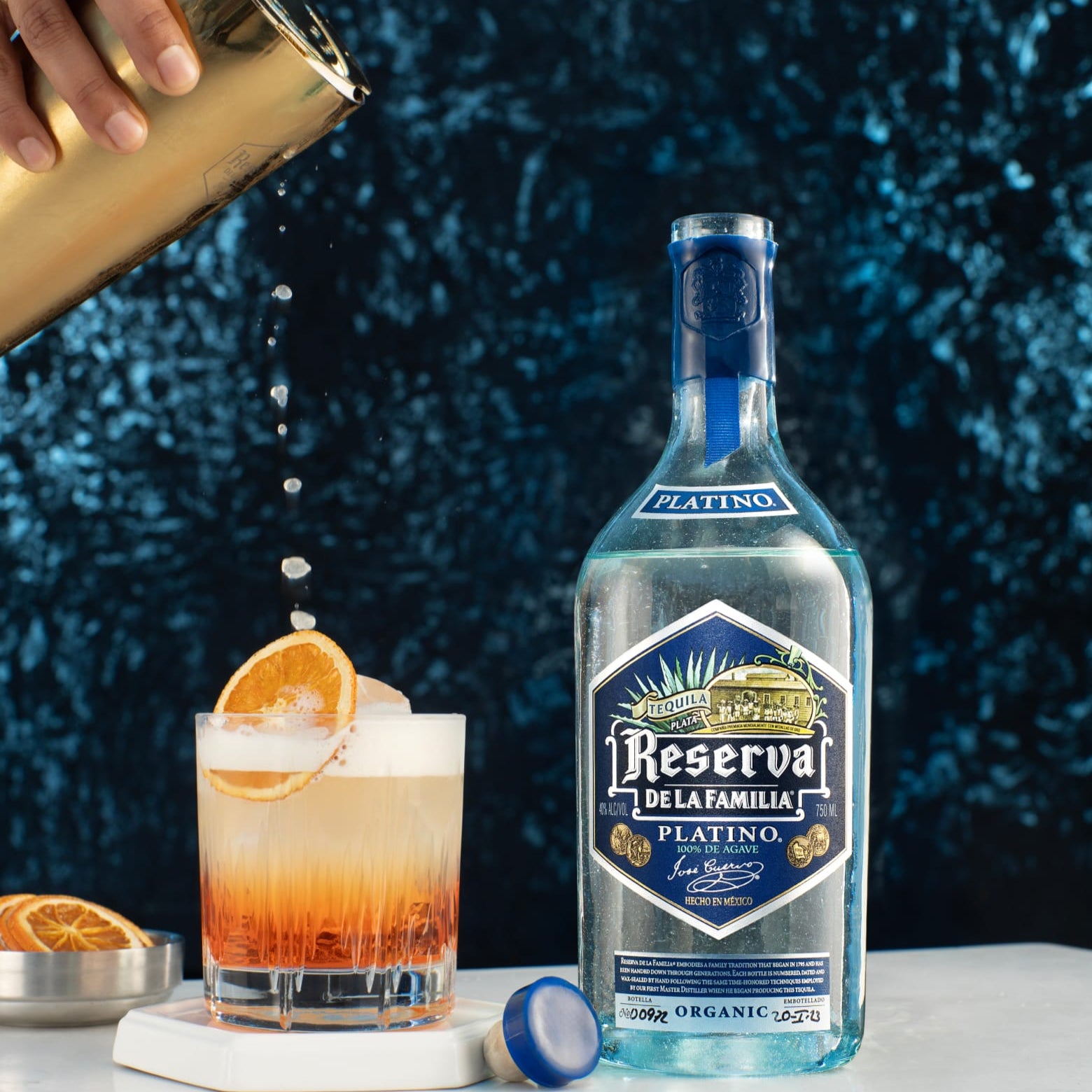 Load image into Gallery viewer, Bottle of Reserva de la Familia Platinio tequila with a cocktail being poured next to it against a dark textured background.