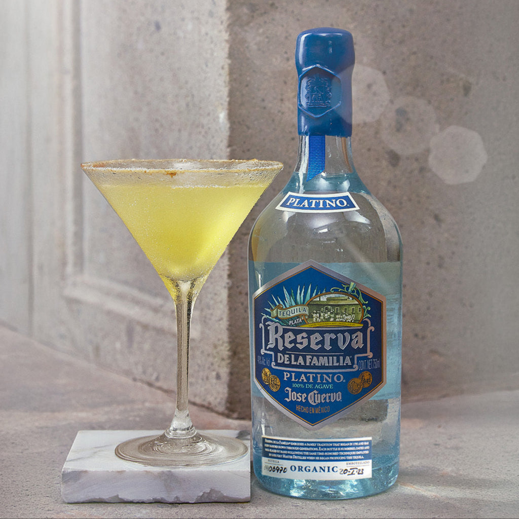 Bottle of Jose Cuervo Reserva de la Familia with a cocktail on a marble coaster against a textured wall.