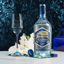 Load image into Gallery viewer, Bottle and glass of Reserva de la Familia Platinio tequila with decorative elements on a dark background