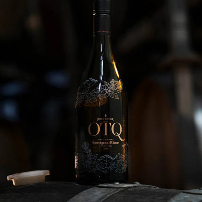 Bottle of OTQ wine on a wooden barrel with barrels in the background
