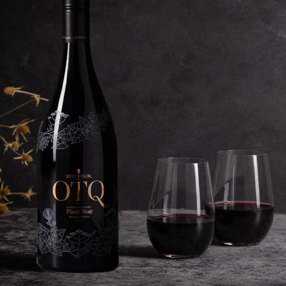 Load image into Gallery viewer, A bottle of Jules_Taylor_OTQ_Pinot_Noir next to two filled wine glasses on a dark surface.