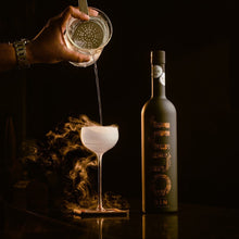 Load image into Gallery viewer, Bottle of Juno Gin with a hand pouring a cocktail into a glass against a dark background