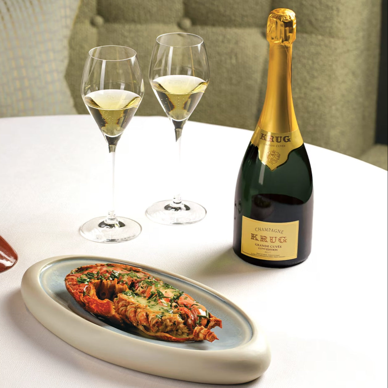 Load image into Gallery viewer, Two glasses of champagne, a bottle of Krug Grande Cuvee champagne, and a dish with food on a table.