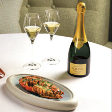 Load image into Gallery viewer, Two glasses of champagne, a bottle of Krug Grande Cuvee champagne, and a dish with food on a table.