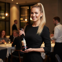 Load image into Gallery viewer, Woman holding a bottle of Kaesler_Old_Bastard_Shiraz wine in a restaurant setting