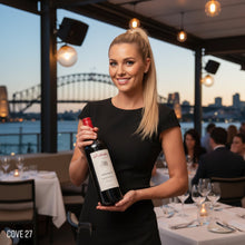 Load image into Gallery viewer, Woman holding a bottle of Kalleske Merchant Cabernet Sauvignon wine in a restaurant with a cityscape view