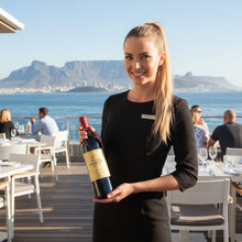 Load image into Gallery viewer, Waitress holding a bottle of Kanonkop Kadette Pinotage wine with Table Mountain in the background
