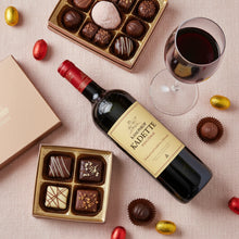 Load image into Gallery viewer, Bottle of Kanonkop Kadette Pinotage wine with chocolates and a glass of red wine on a textured surface.