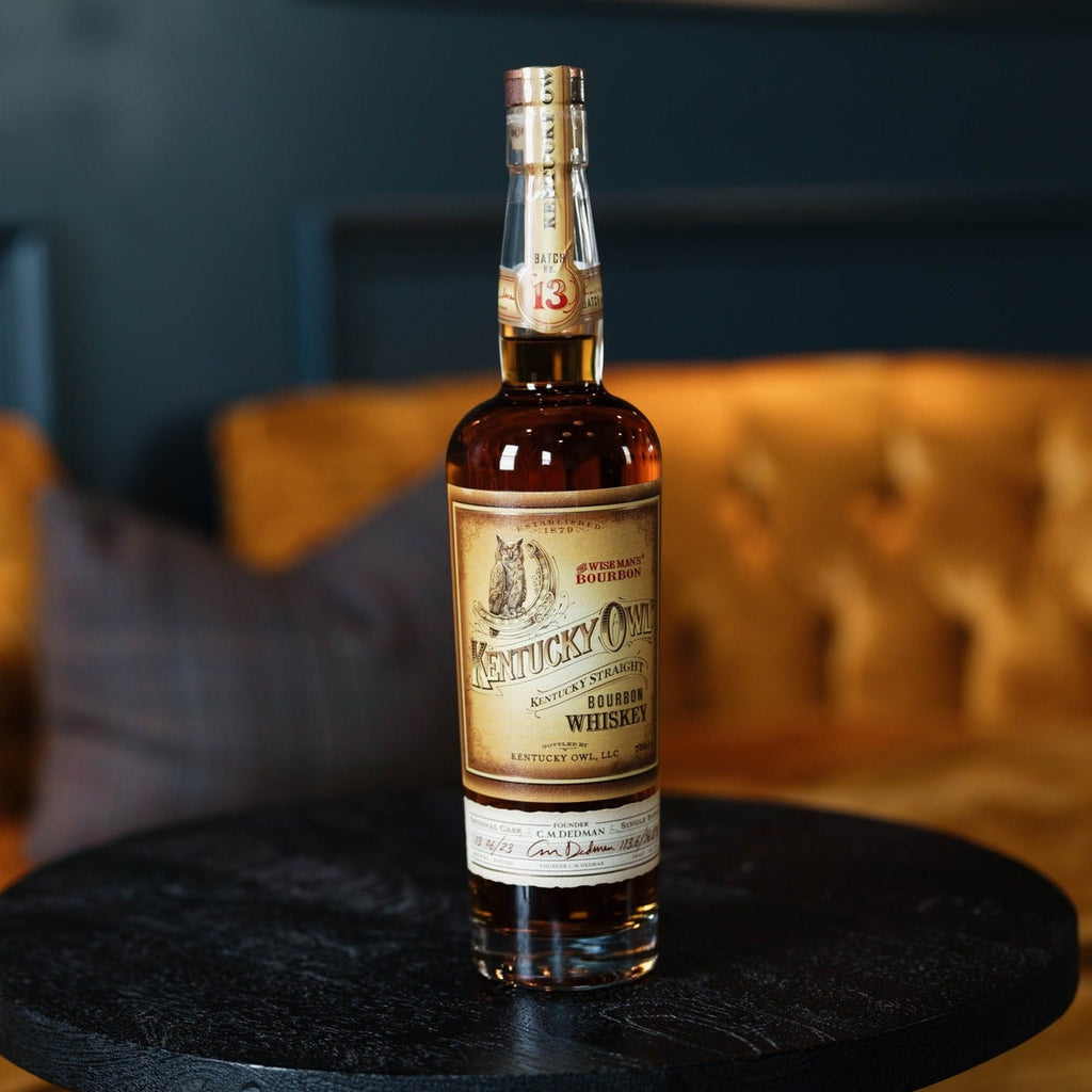 Bottle of Kentucky Owl Batch Bourbon on a black round table with a blurred background