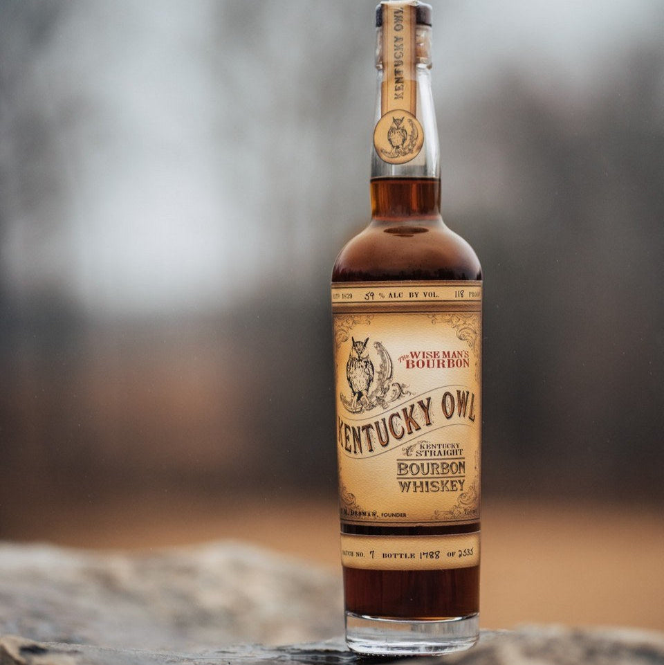 Load image into Gallery viewer, Bottle of Kentucky Owl bourbon whiskey on a rock with a blurred background.