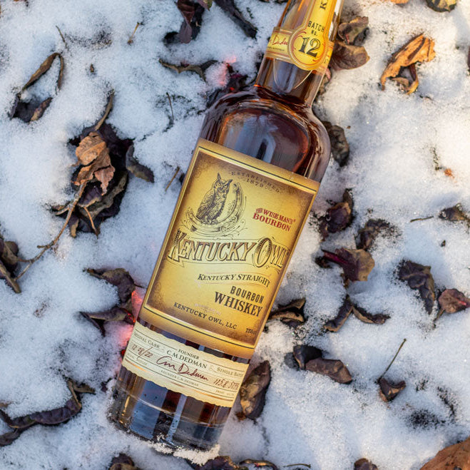 Bottle of Kentucky Old Fashioned Whiskey on a snowy ground with leaves.