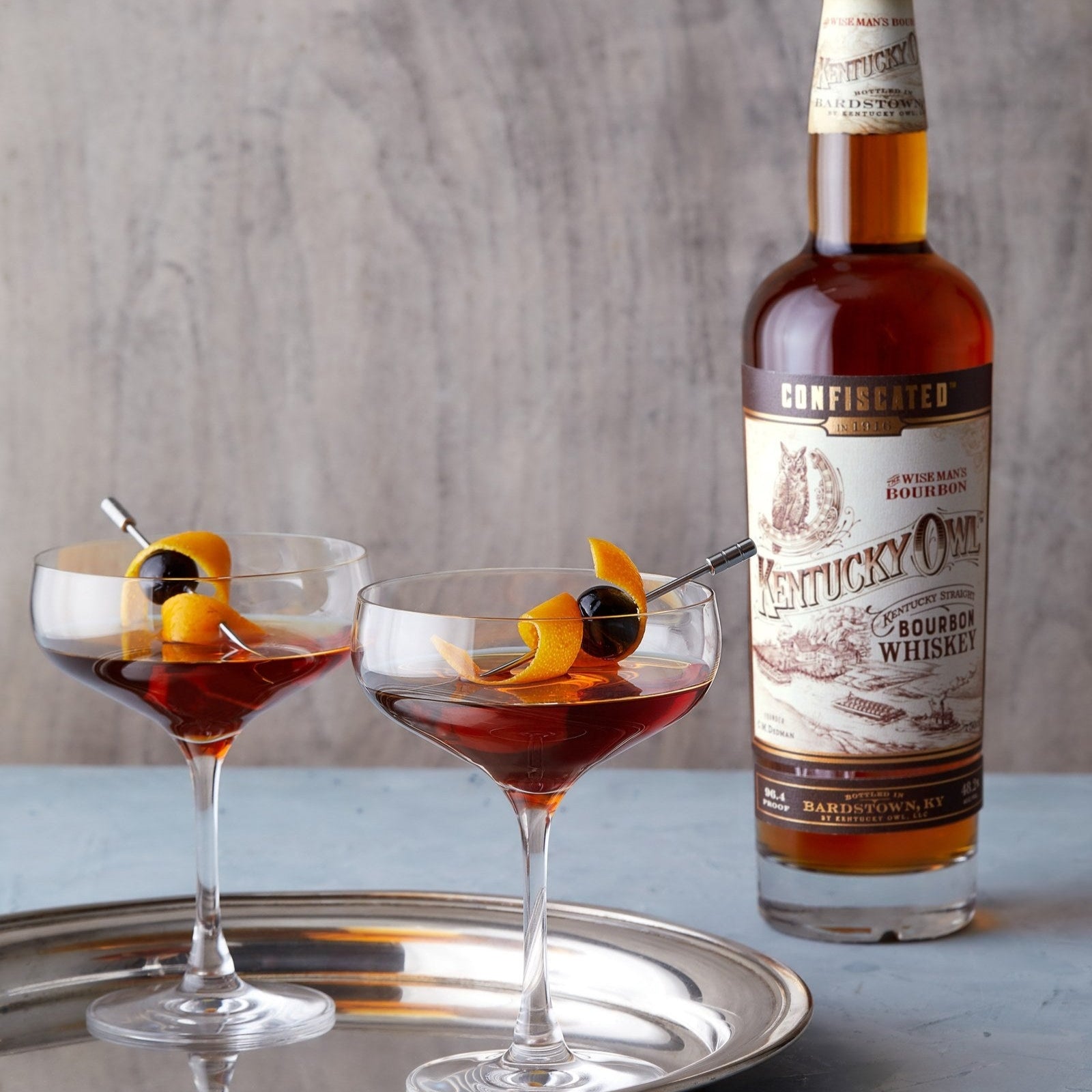 Load image into Gallery viewer, Two cocktail glasses with bourbon and garnishes on a tray with a bottle of bourbon.