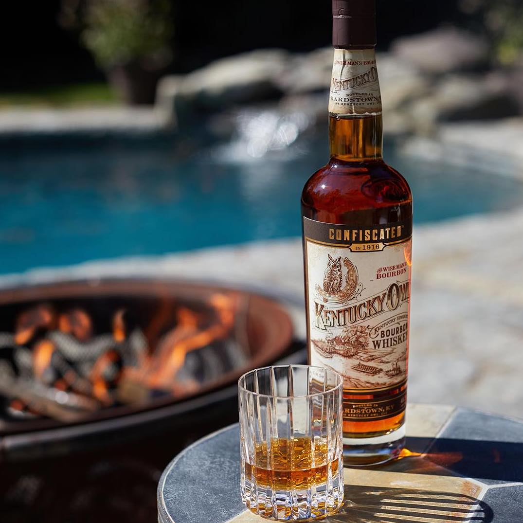 Load image into Gallery viewer, Bottle of Kentucky Old Whiskey and glass on a table by a fire pit.