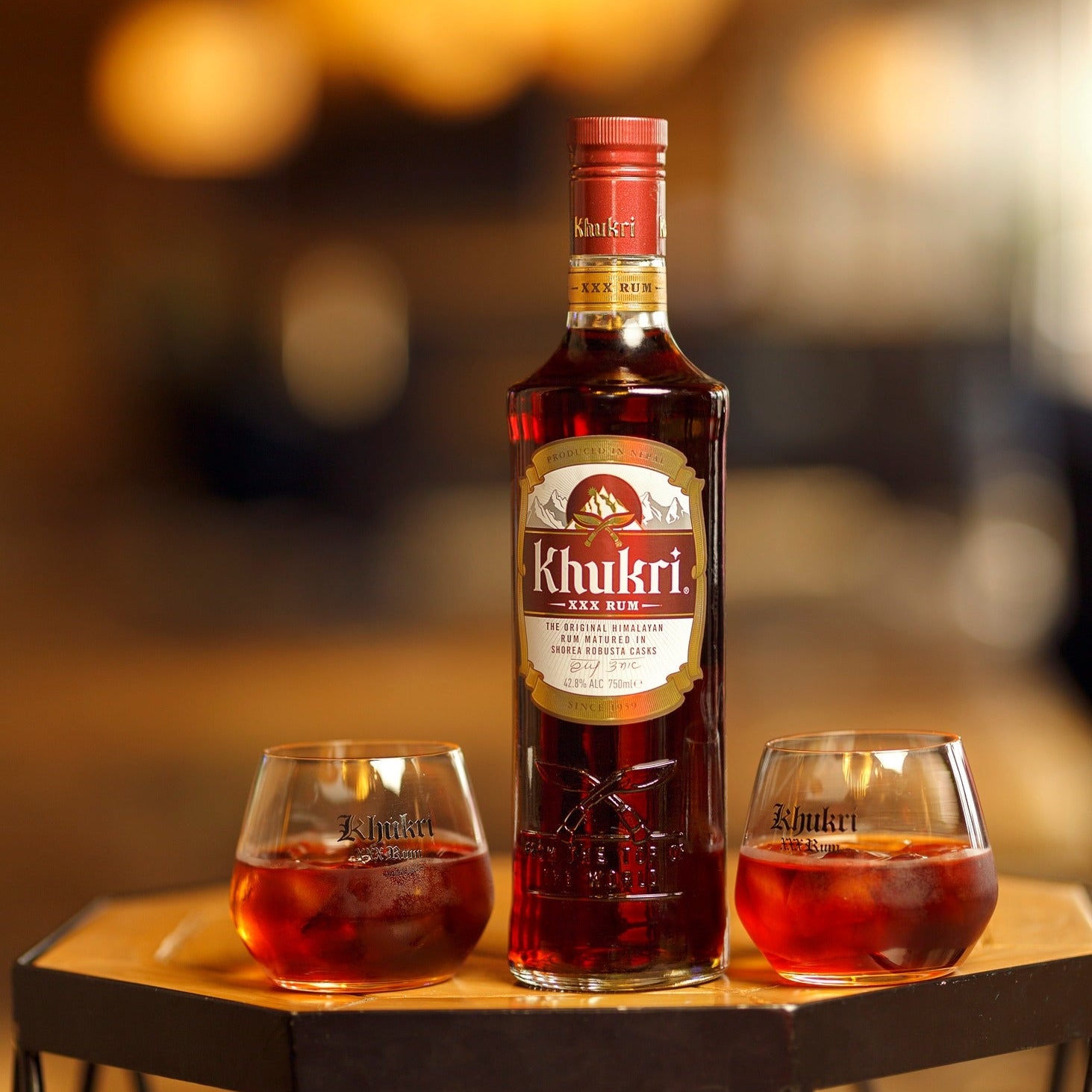 Load image into Gallery viewer, Khukri dark rum bottle with two glasses of red liquid on a blurred background