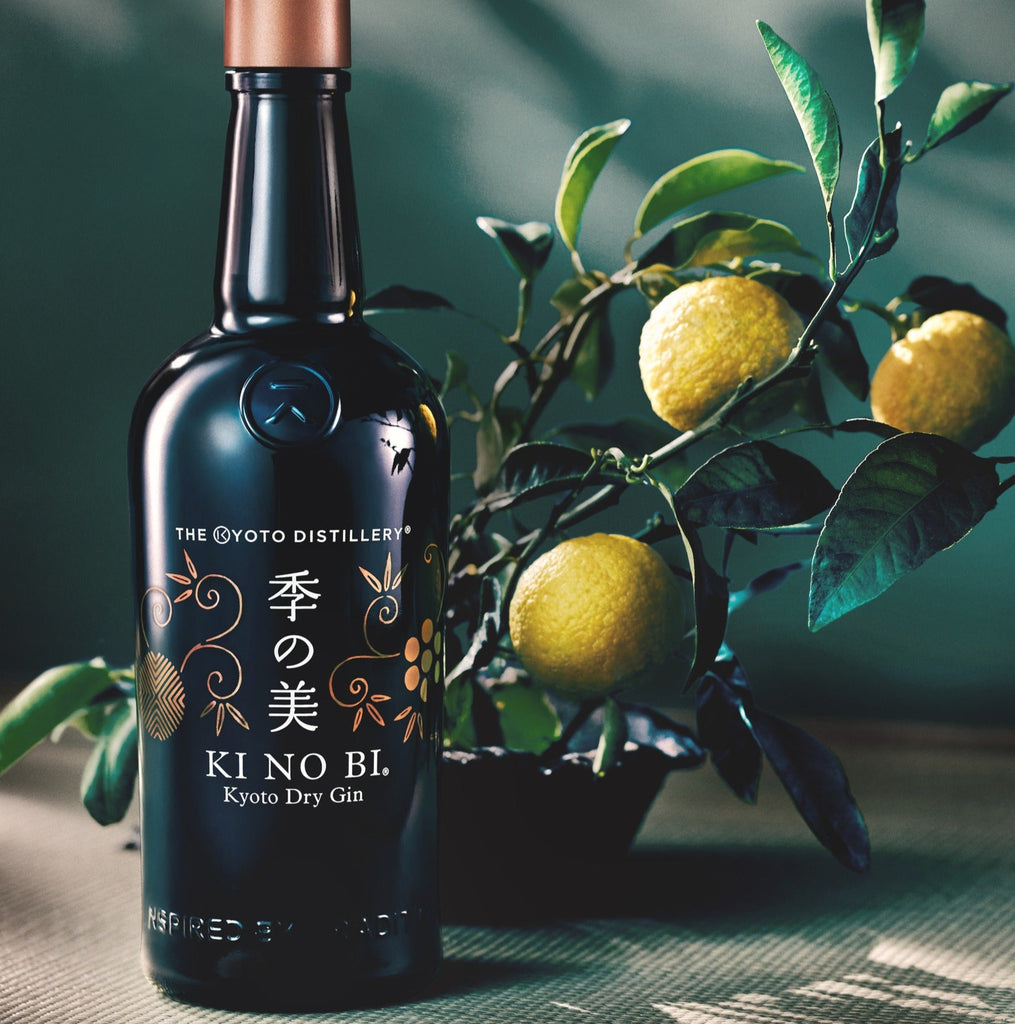 Bottle of KI NO BI Kyoto Dry Gin with a branch of lemons and leaves on a textured surface.