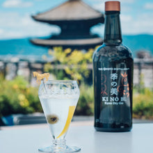 Load image into Gallery viewer, Bottle of KI NO BI gin with a cocktail garnished with a lemon peel against a scenic background.