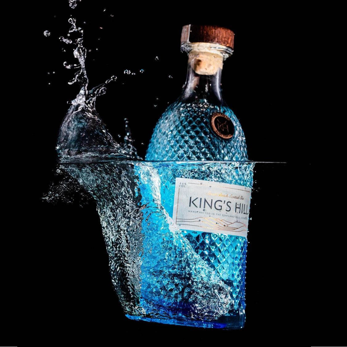 Load image into Gallery viewer, A King's Hill Scottish Gin bottle with a cork stopper, shown partially submerged in splashing water against a solid black background.