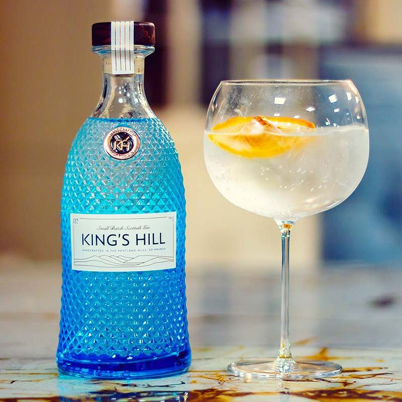 Load image into Gallery viewer, Blue bottle of King's Hill gin with a glass of gin and tonic on a table.