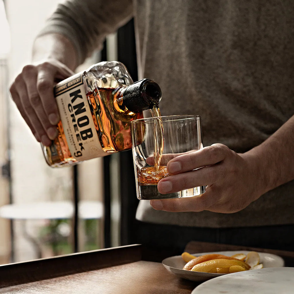 Person pouring whiskey into a glass with a bottle label visible.