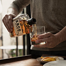 Load image into Gallery viewer, Person pouring whiskey into a glass with a bottle label visible.