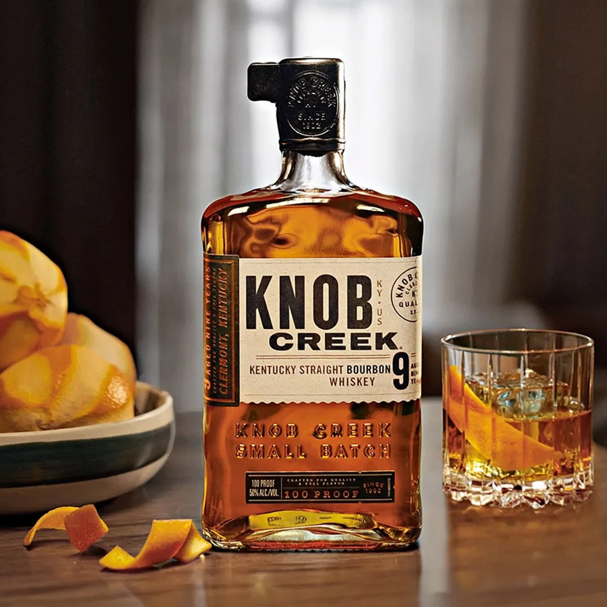 Load image into Gallery viewer, Bottle of Knob Creek bourbon whiskey with a glass of whiskey and oranges on a wooden surface.