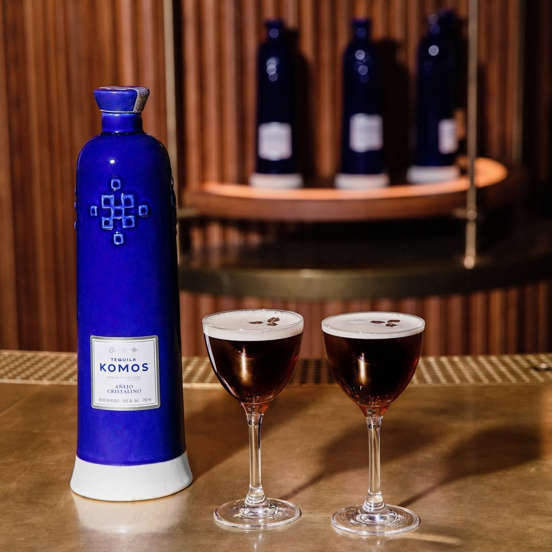 Load image into Gallery viewer, Bottle of Komos Añejo Cristalino Tequila with two glasses on a bar counter