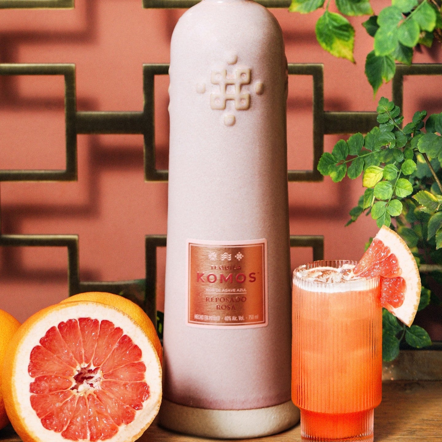 Load image into Gallery viewer, Bottle of Komos Reposado Rosa Tequila with a glass of pink cocktail and grapefruit on a decorative background