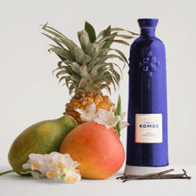 Load image into Gallery viewer, Komos Anejo Cristalino Tequila in its deep blue artisan ceramic bottle next to tropical fruits of pineapple and mango