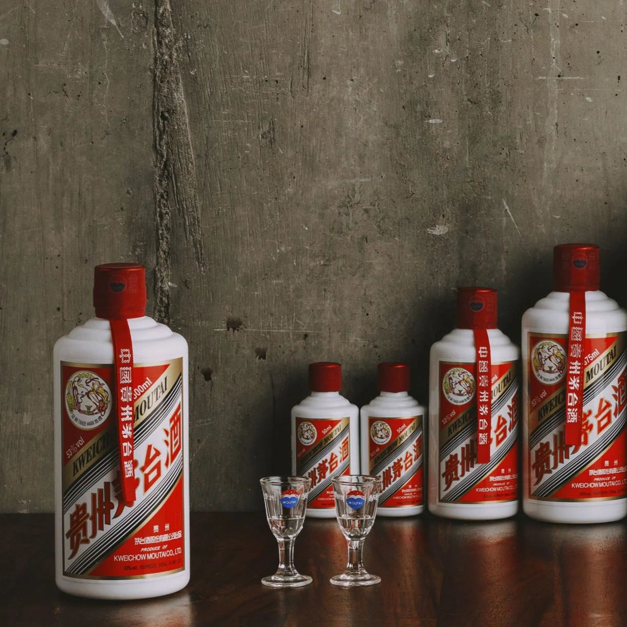 Load image into Gallery viewer, Row of red and white bottles with a gray concrete wall background