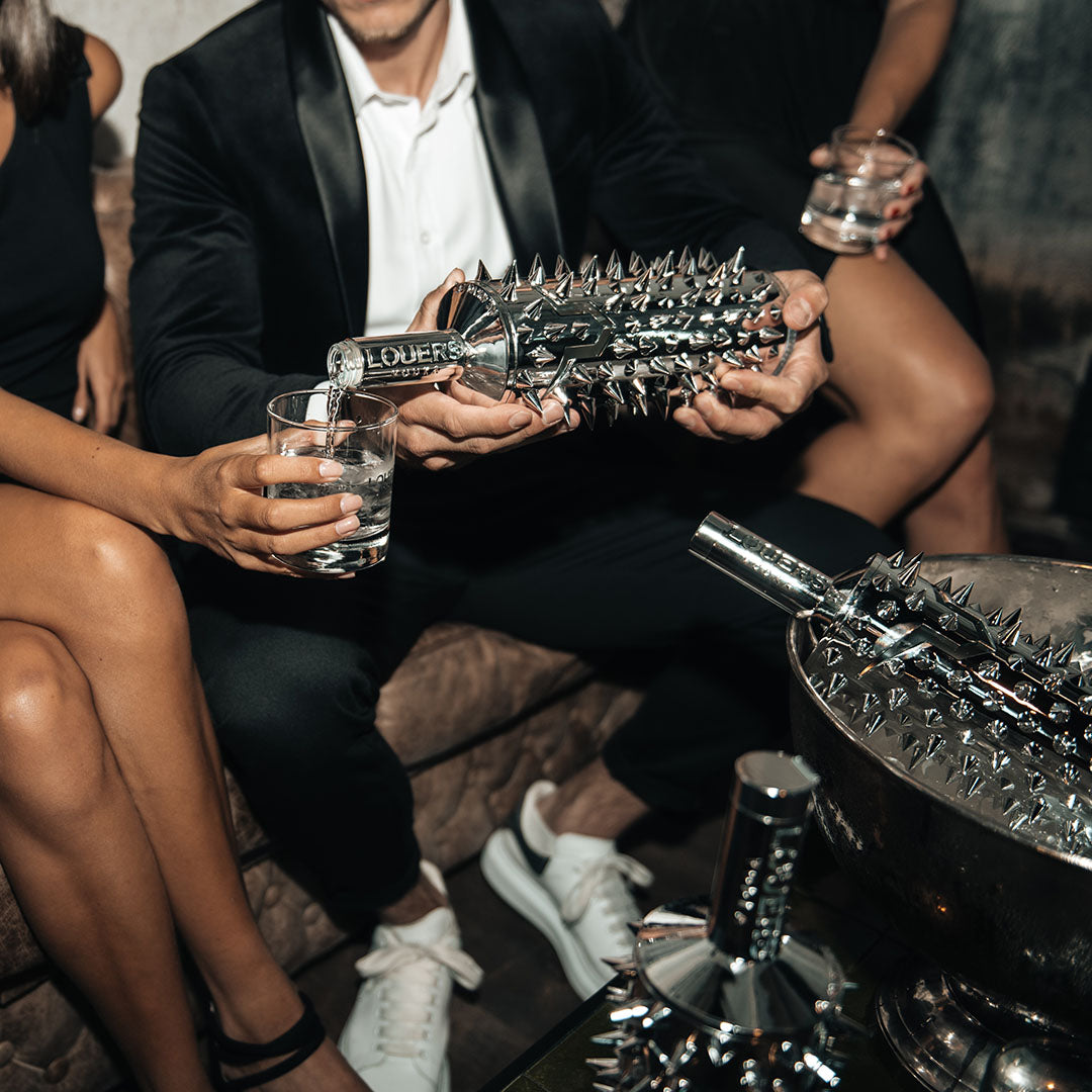 Load image into Gallery viewer, Person pouring a spiked bottle of Louers Vodka into a glass with others around