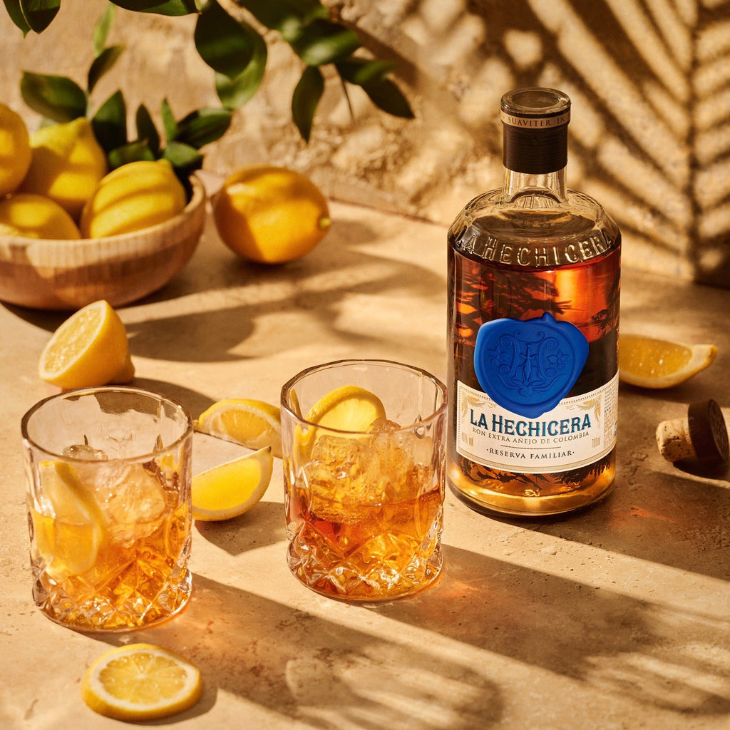 Bottle of La Hechicera Fine Aged Dark Rum  with two glasses of cocktail on a wooden surface with lemons.