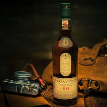 Load image into Gallery viewer, Bottle of Lagavulin whisky with a camera and leather bag on a wooden surface