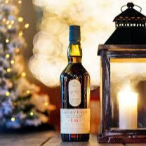 Load image into Gallery viewer, Bottle of Lagavulin whiske on a wooden surface with a blurred festive background