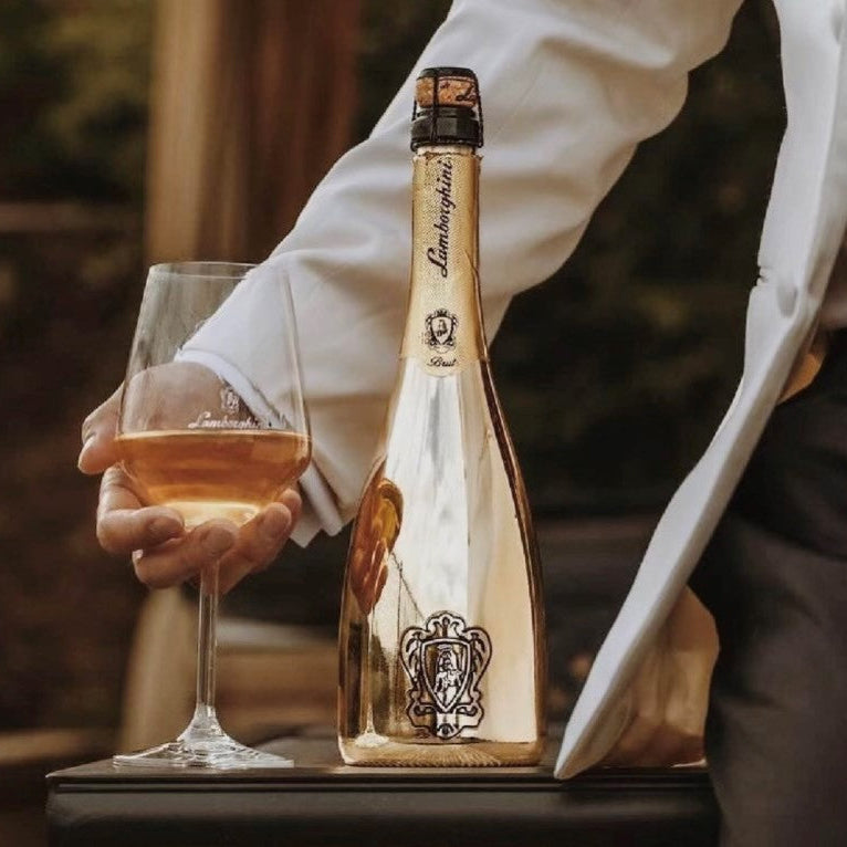 Load image into Gallery viewer, Bottle of Lamborghini V12 Brut Vino Spumante being held by a person with a glass of champagne.