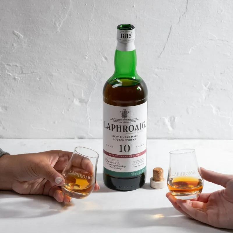 Load image into Gallery viewer, A bottle of Laphroaig 10YO Sherry Oak Finish Whisky on a white table and two hands with glasses full of neat whisky