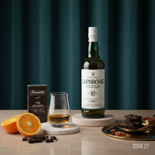 Load image into Gallery viewer, Laphroaig 10-year-old whiskey bottle with a glass of whiskey, oranges, and chocolate on a wooden table.
