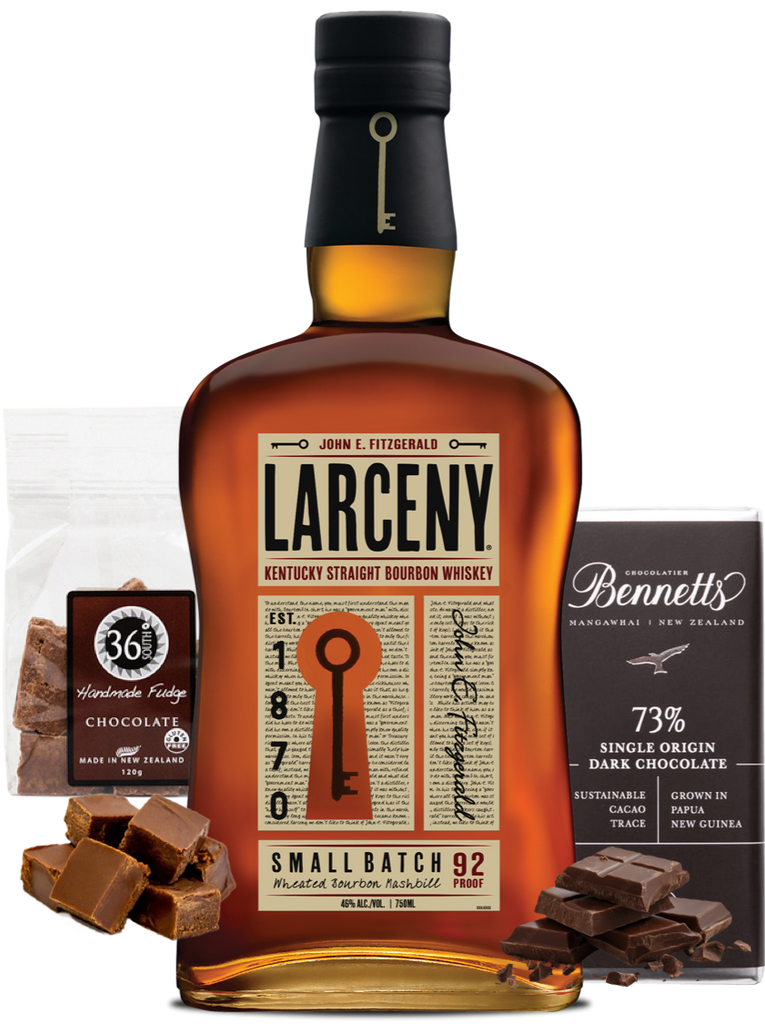 A bottle of Larceny Kentucky Straight Bourbon Whiskey centred on a white background, flanked by a bag of 36 Degrees Chocolate handmade fudge and a bar of Bennett's 73% Single Origin Dark Chocolate, with pieces of chocolate scattered in front.
