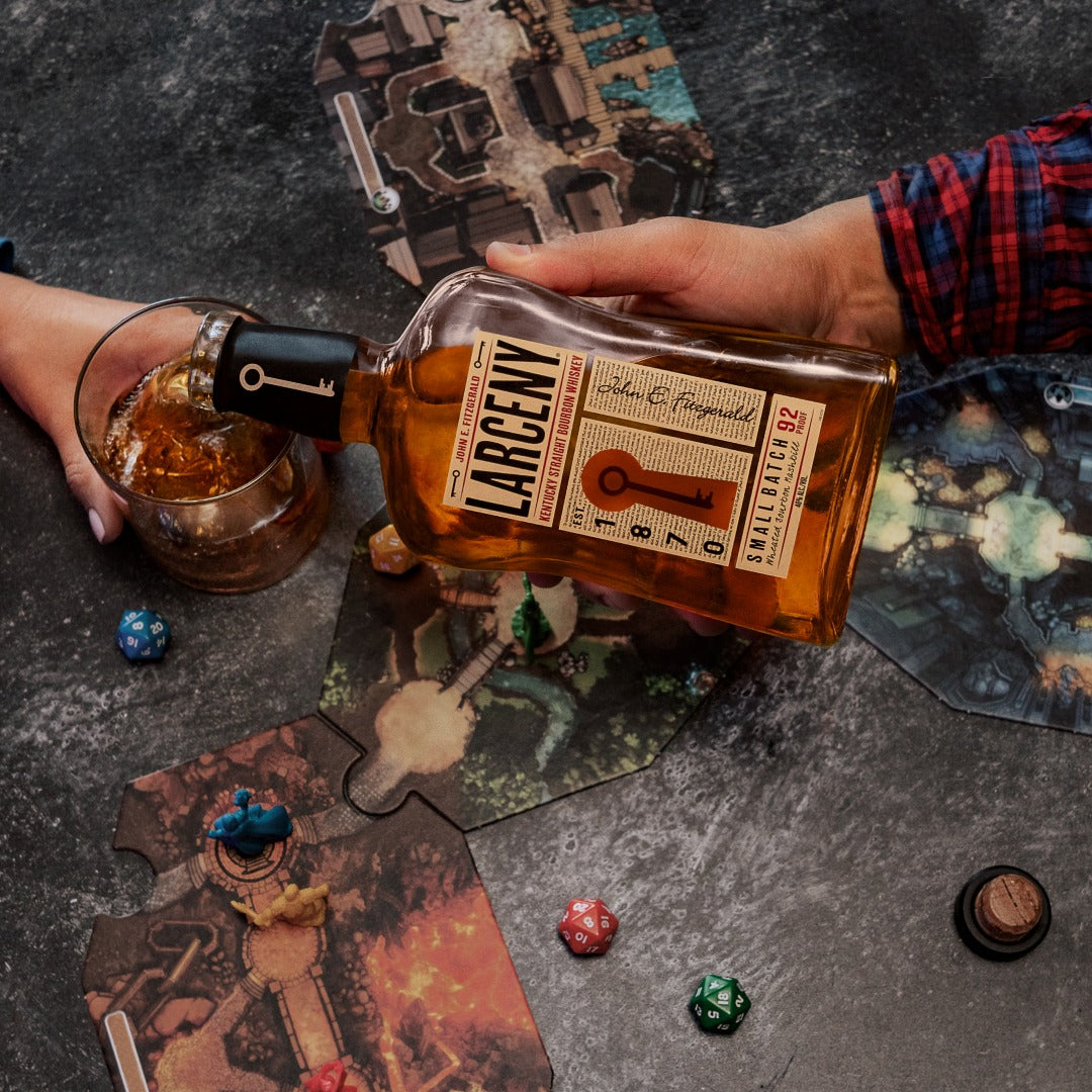 Load image into Gallery viewer, A man pouring some Larceny Kentucky Straight Bourbon Whiskey into a glass that is standing on a dark coloured table