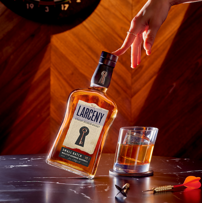 Load image into Gallery viewer, A woman reaching for a bottle of Larceny Kentucky Straight Bourbon Whiskey that is standing on marble table 