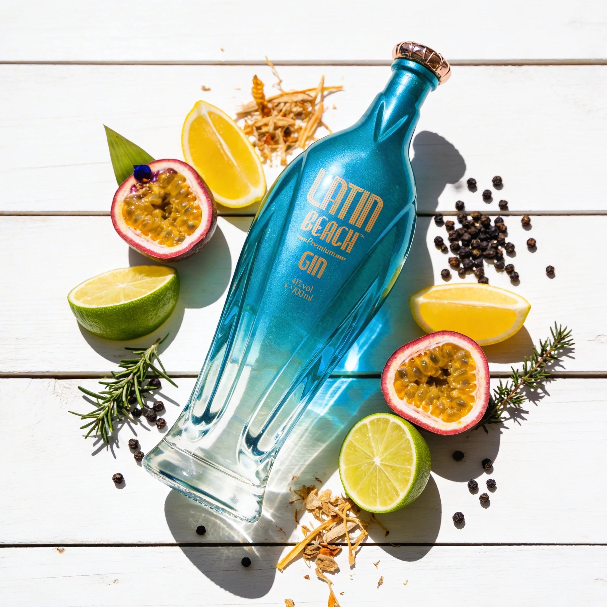 Load image into Gallery viewer, Blue bottle of Latin Beach Gin surrounded by tropical fruits, citrus and herbs on a wooden surface
